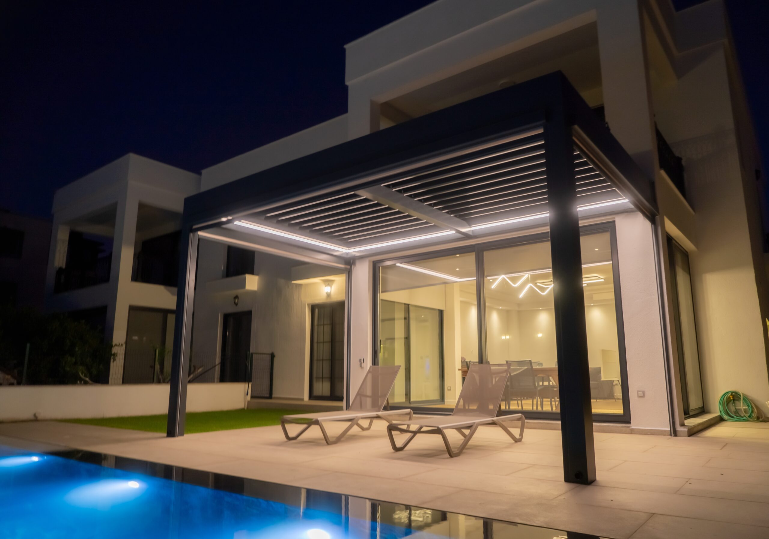 Moderne Pergola mit LED-Beleuchtung am Abend neben Pool und Terrasse